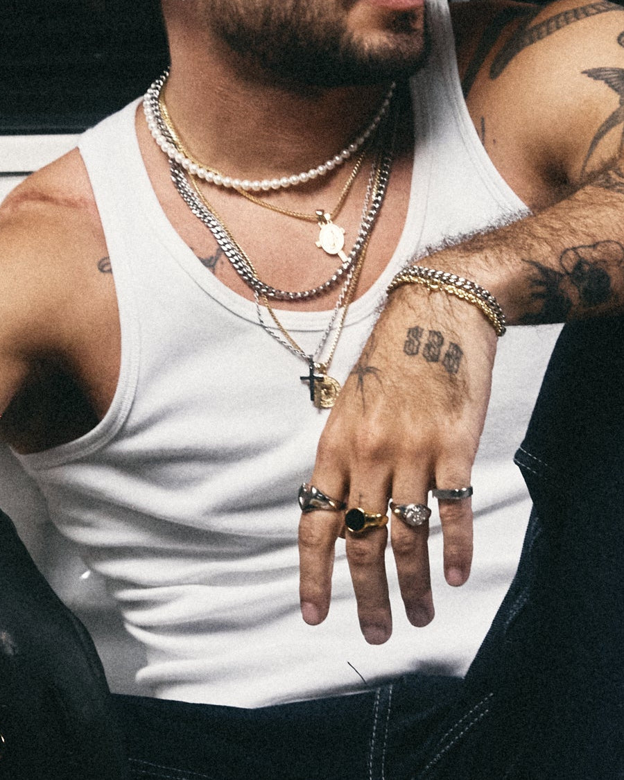 detalle de cadenas doradas y plateadas con perlas, y anillos de ambos tonos sobre una camiseta blanca