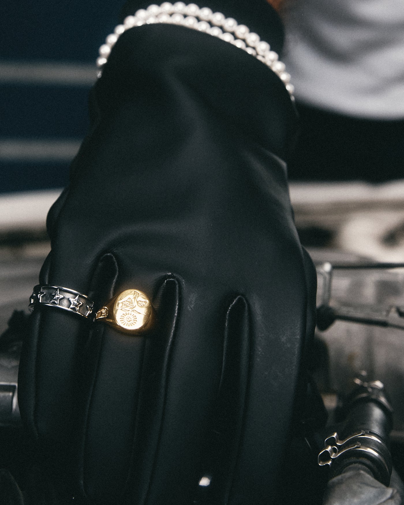 detalle de un anillo plateado y uno dorado sobre un guante negro, con perlas en la muñeca