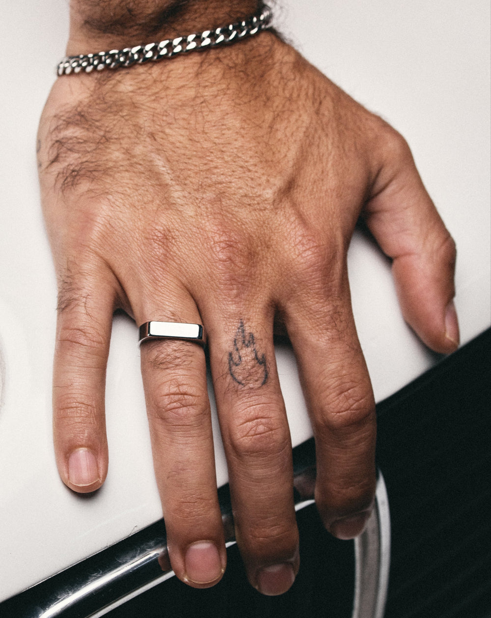 pulsera cubana y anillo slim plateados en una mano apoyada sobre un carro