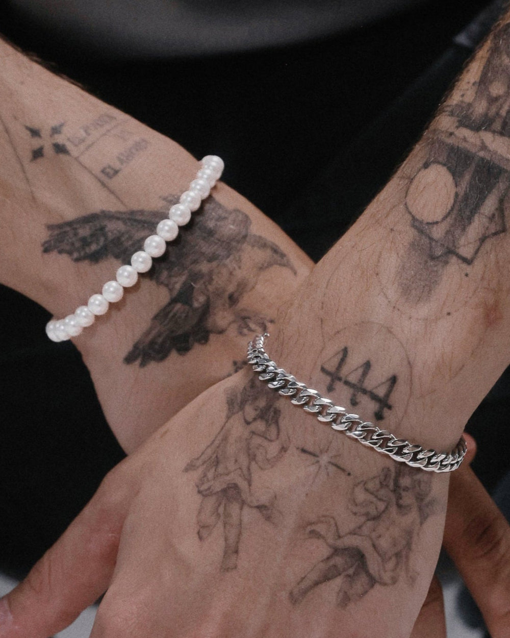 pulsera cubana plateada en una muñeca y pulsera de perlas en la otra